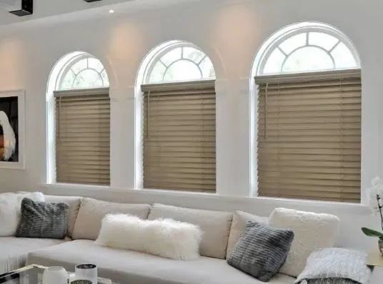 Bright living room with arched windows, beige blinds, and a light-colored sofa with cushions.