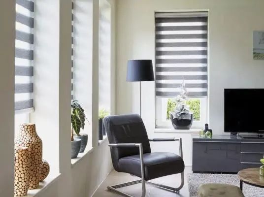 Modern living room with gray chair, black floor lamp, striped shades, and TV on a console