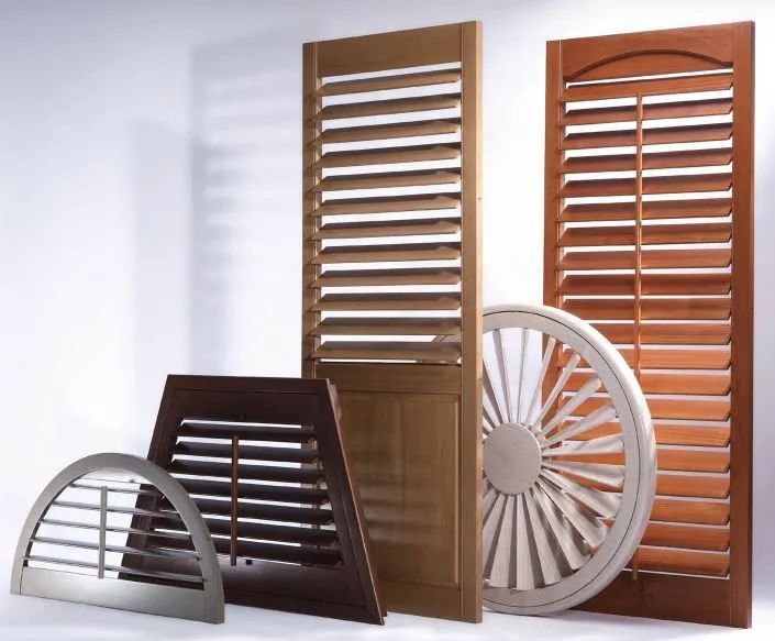 Assorted wooden and white window shutters displayed upright and leaning on a floor against a light wall