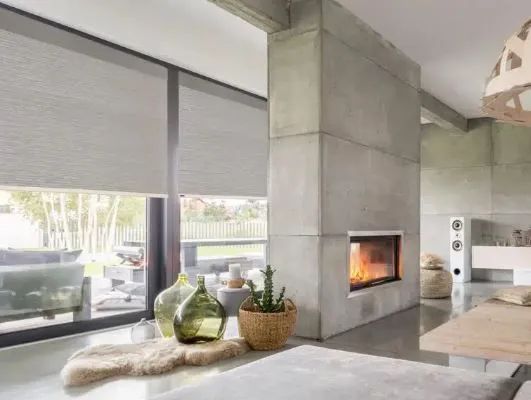 Modern living room with a concrete fireplace, large windows, and a low table with decorative vases.