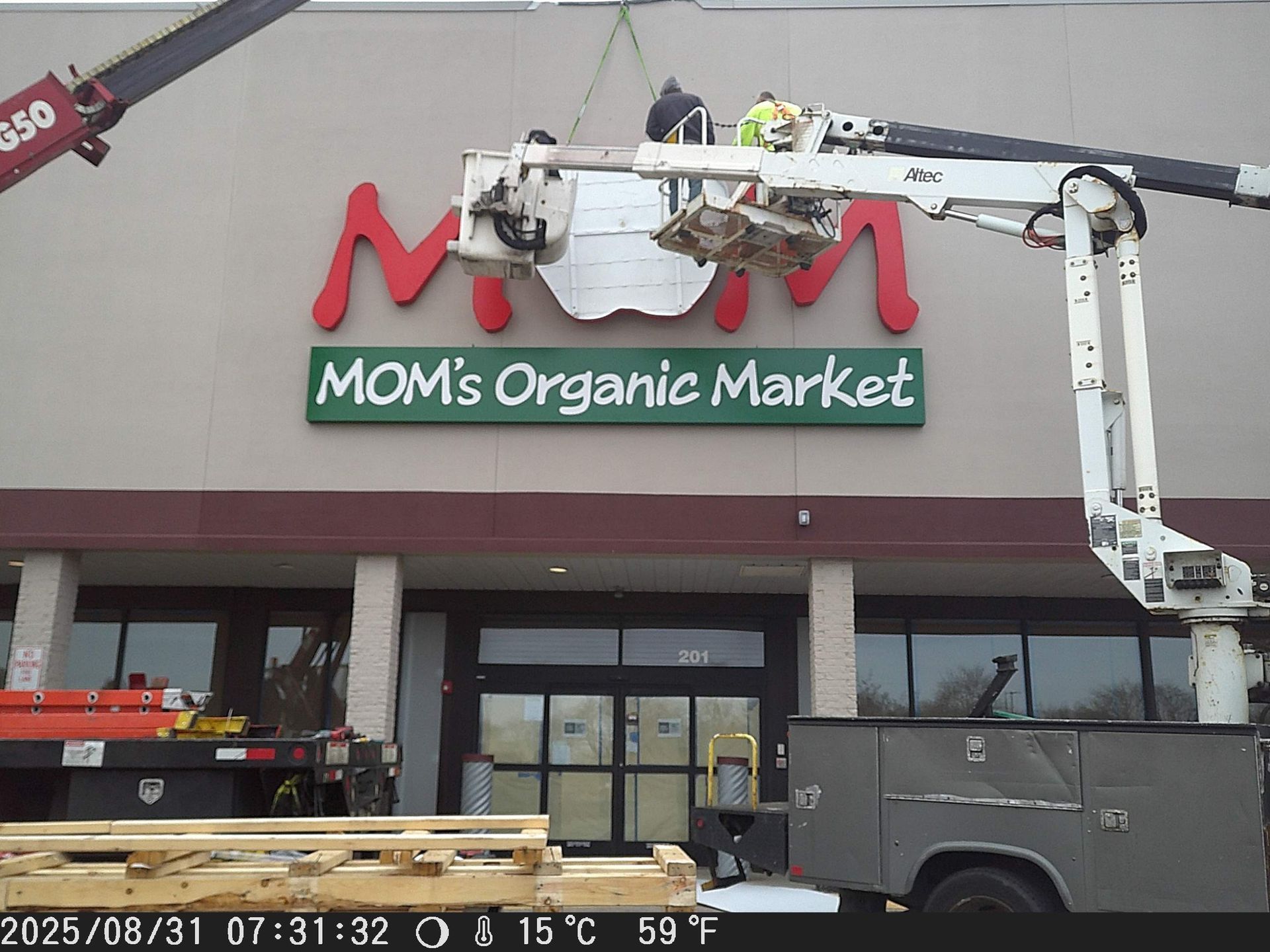 Bucket lift removing red MOM’s Organic Market sign from storefront