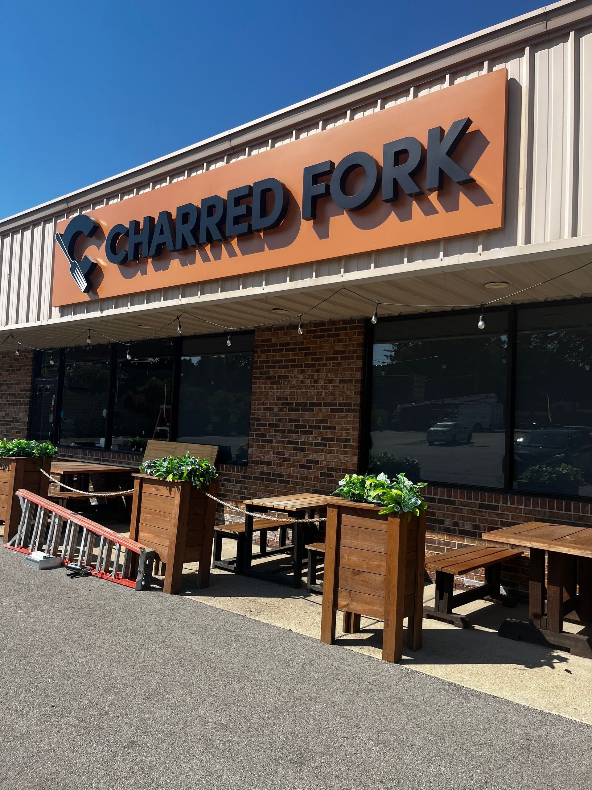 Charred Fork restaurant storefront with orange sign, outdoor tables, and potted plants under a striped awning