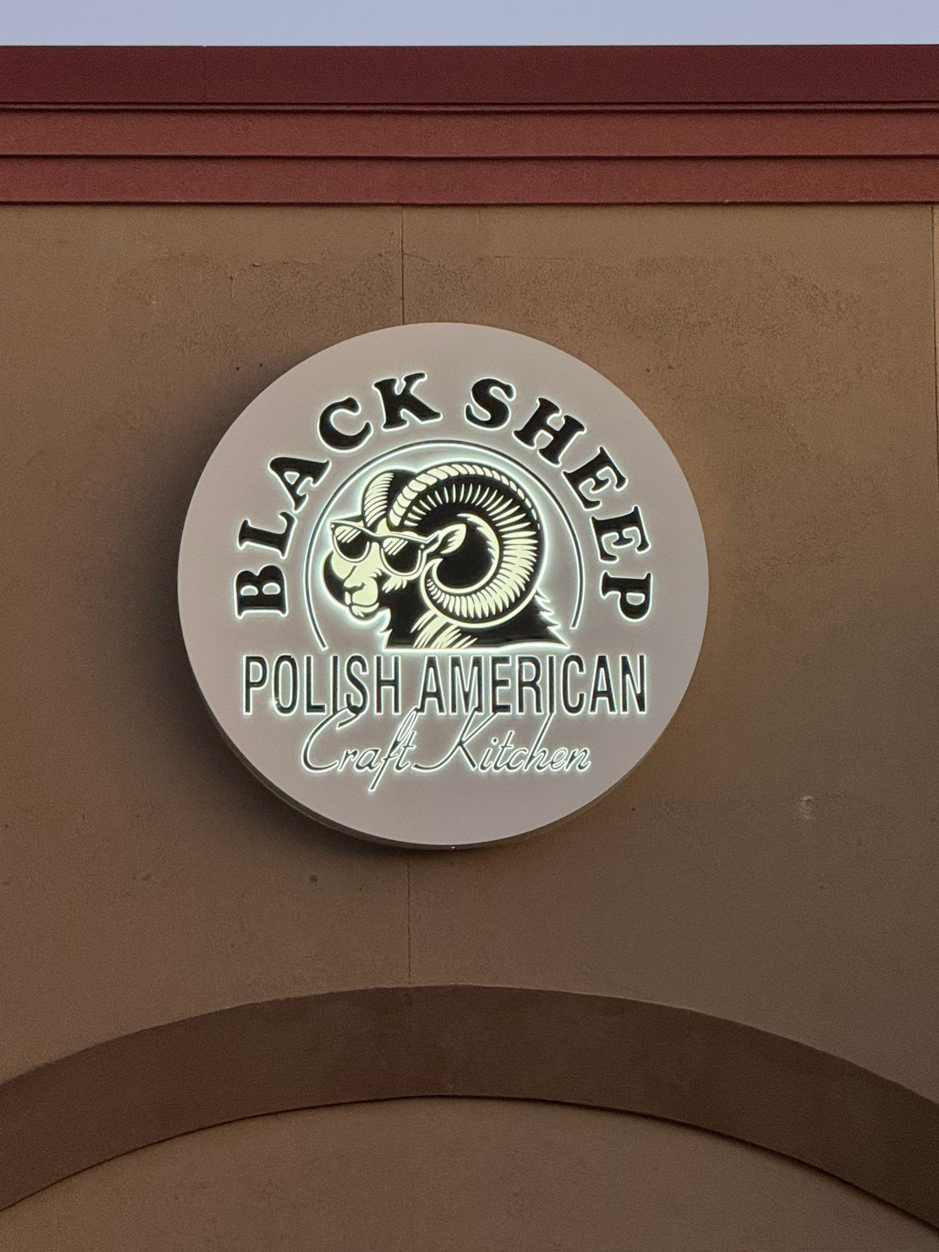 Black Sheep Food Truck logo sign on a tan wall, with a sheep illustration and black-and-white text