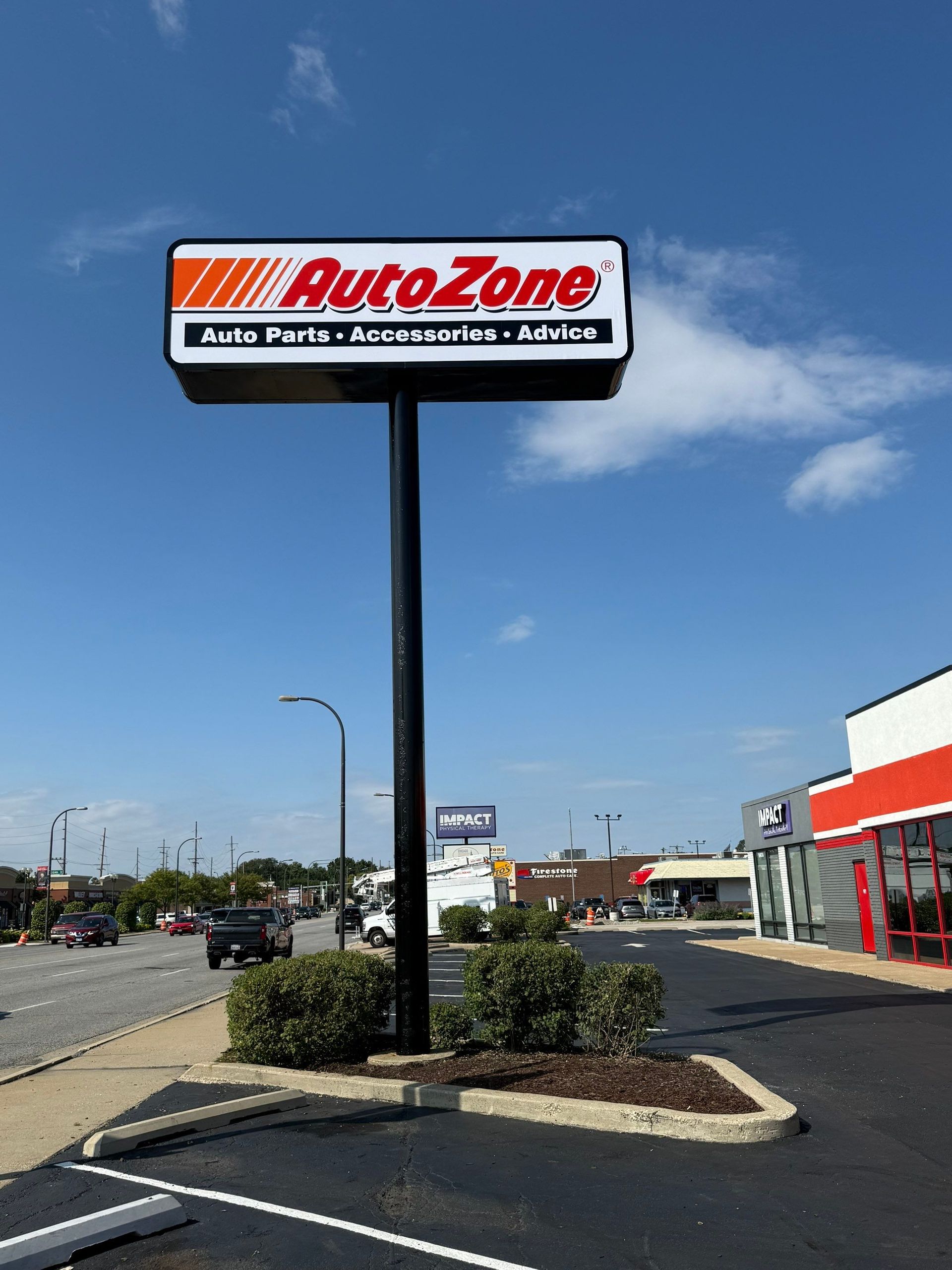 AutoZone roadside sign in a strip mall parking lot under a blue sky