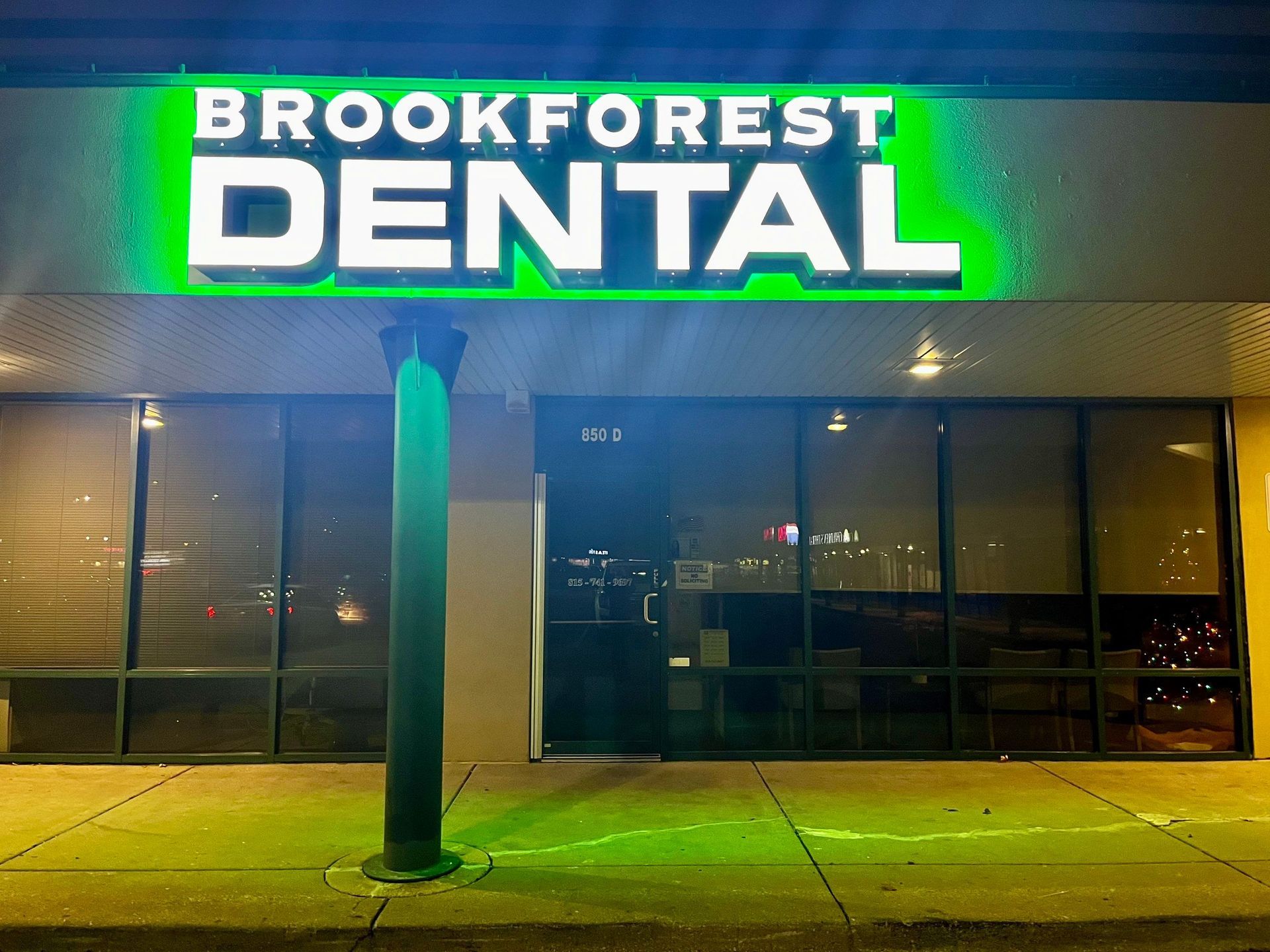 Brookforest Dental storefront at night with bright green and white illuminated sign