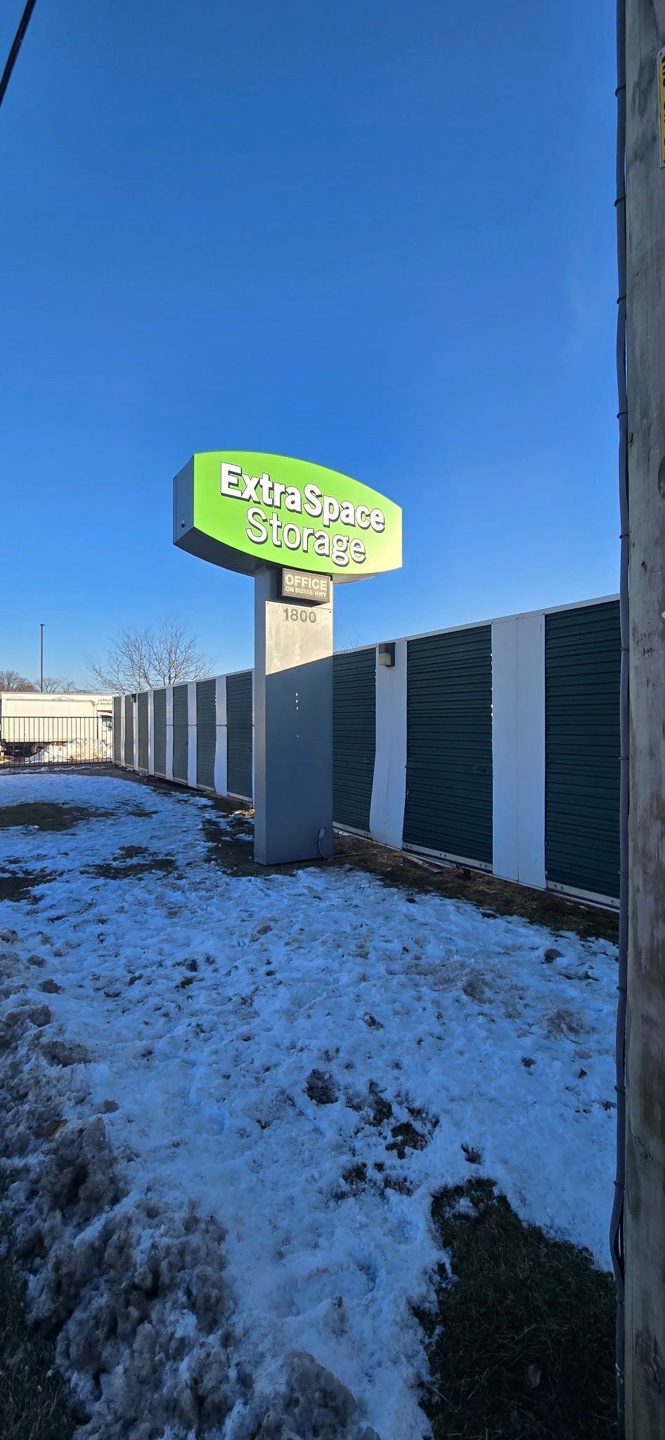 Snowy roadside with a green business sign under a clear blue sky.