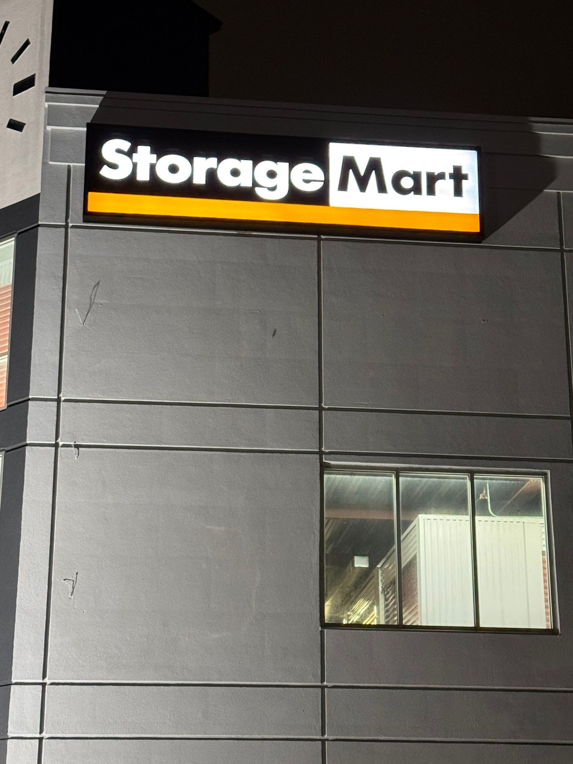 StorageMart sign on a dark building exterior with a lit window below