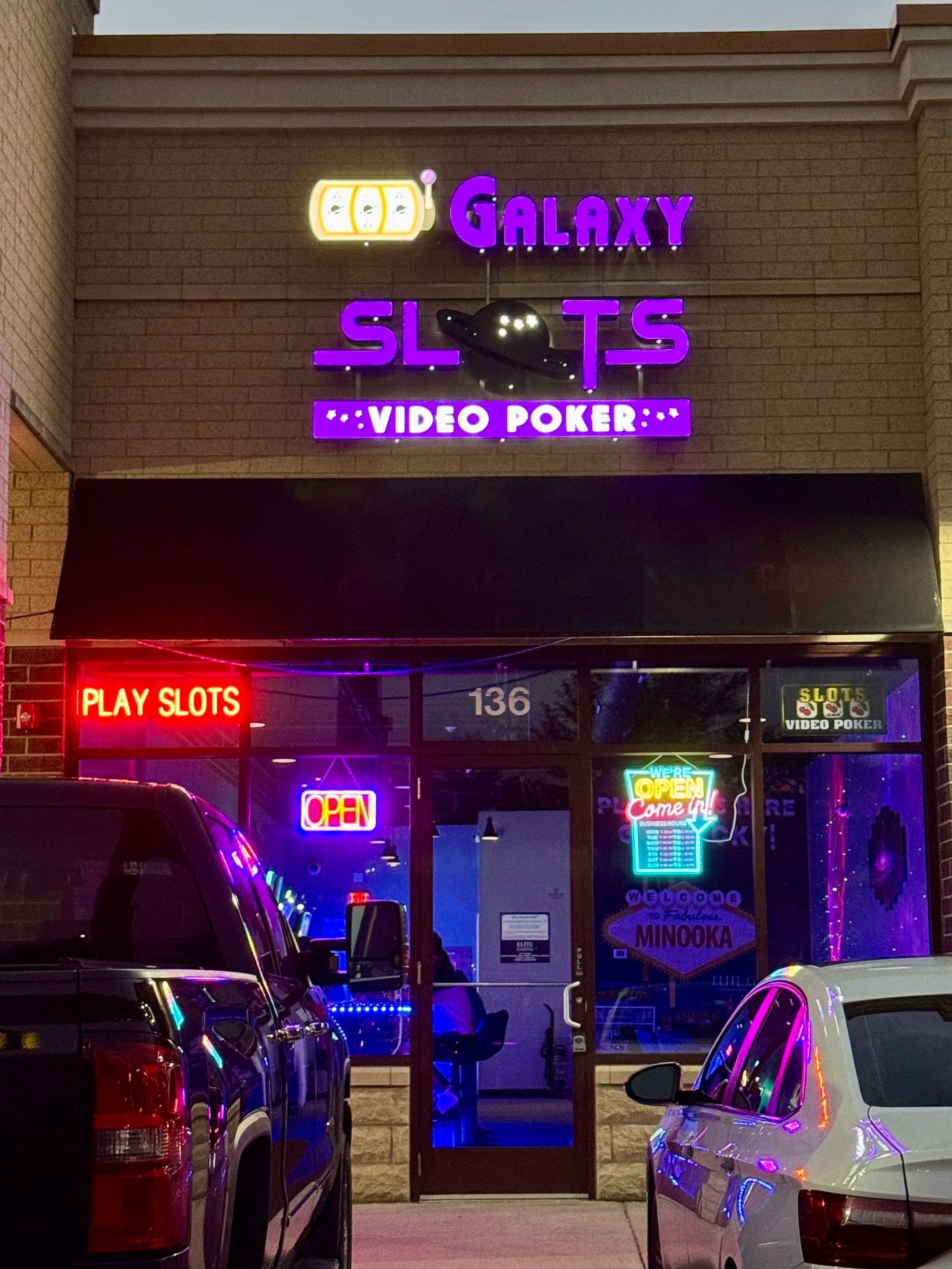 Neon-lit Galaxy SLT Video Poker storefront at night with parked cars outside.