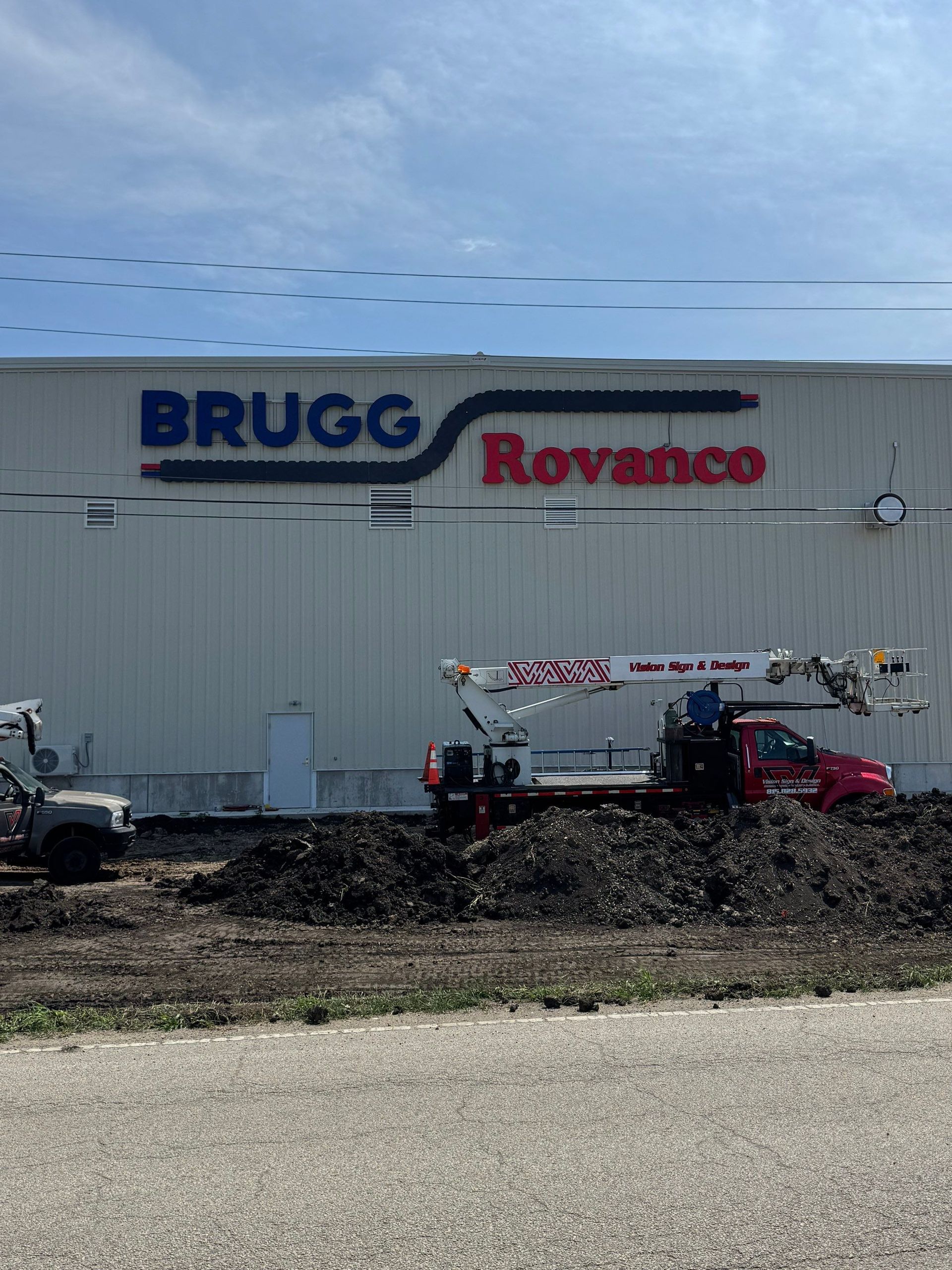 BRUGG Roxtec building with parked utility vehicles and an excavator in front under a blue sky