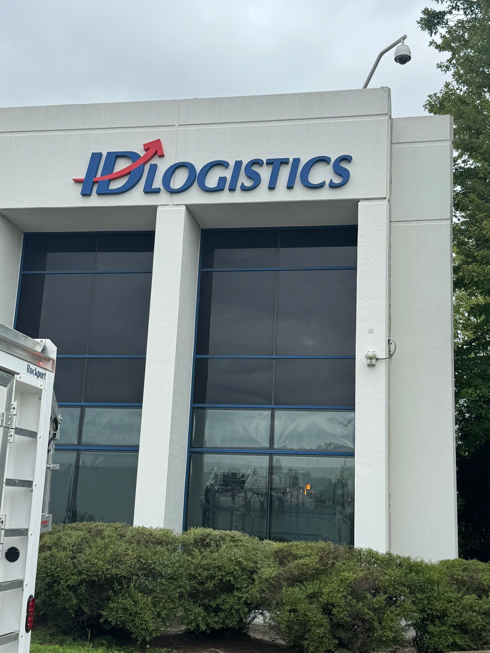 ID Logistics office building exterior with blue and red logo above dark windows and trimmed bushes in front