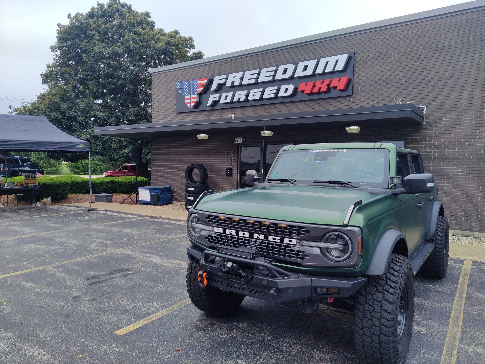 Green off-road Jeep parked outside Freedom Four-Way shop under an awning