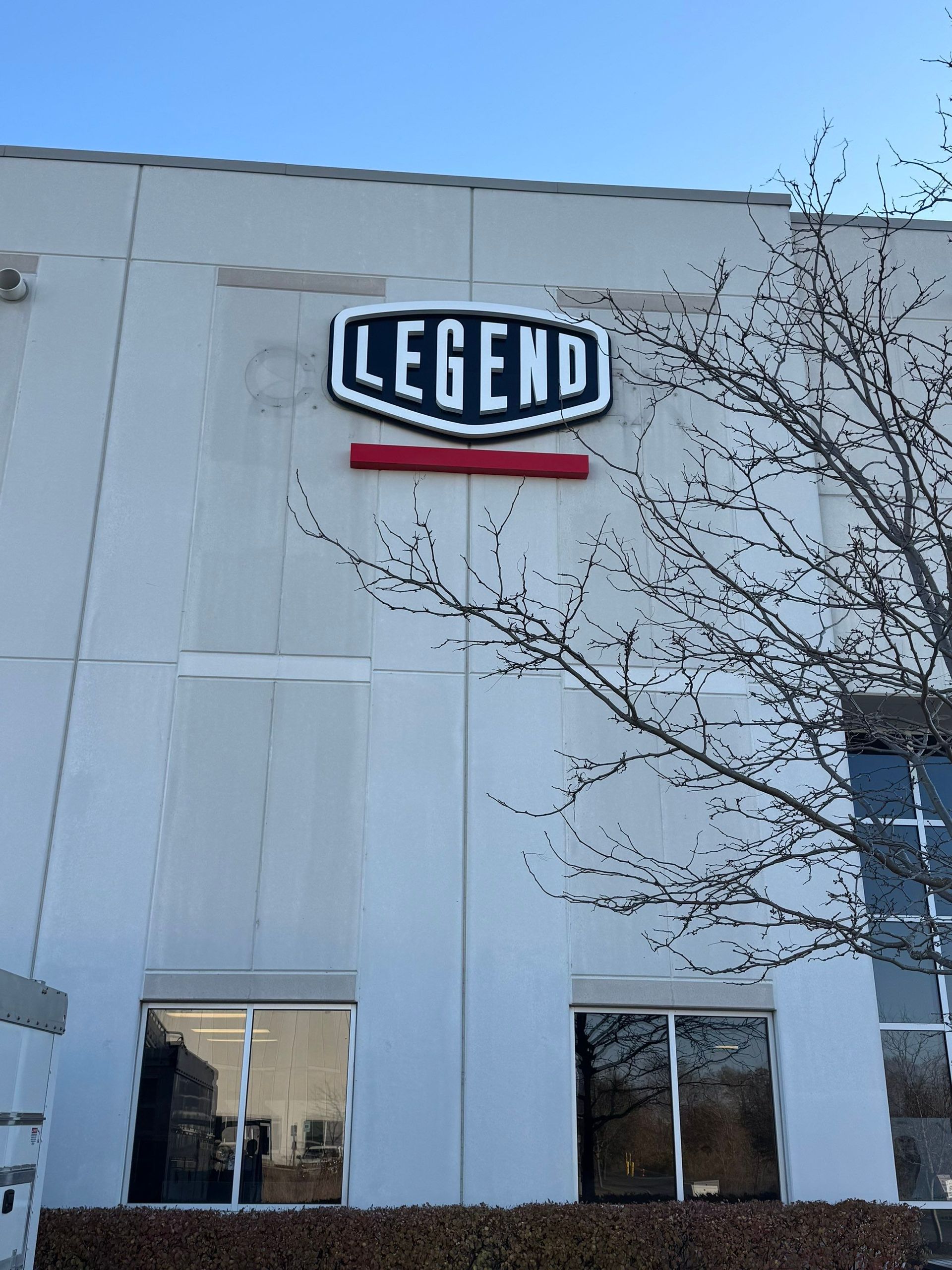 White building exterior with a “LEGEND” sign near the top and bare tree branches in front.