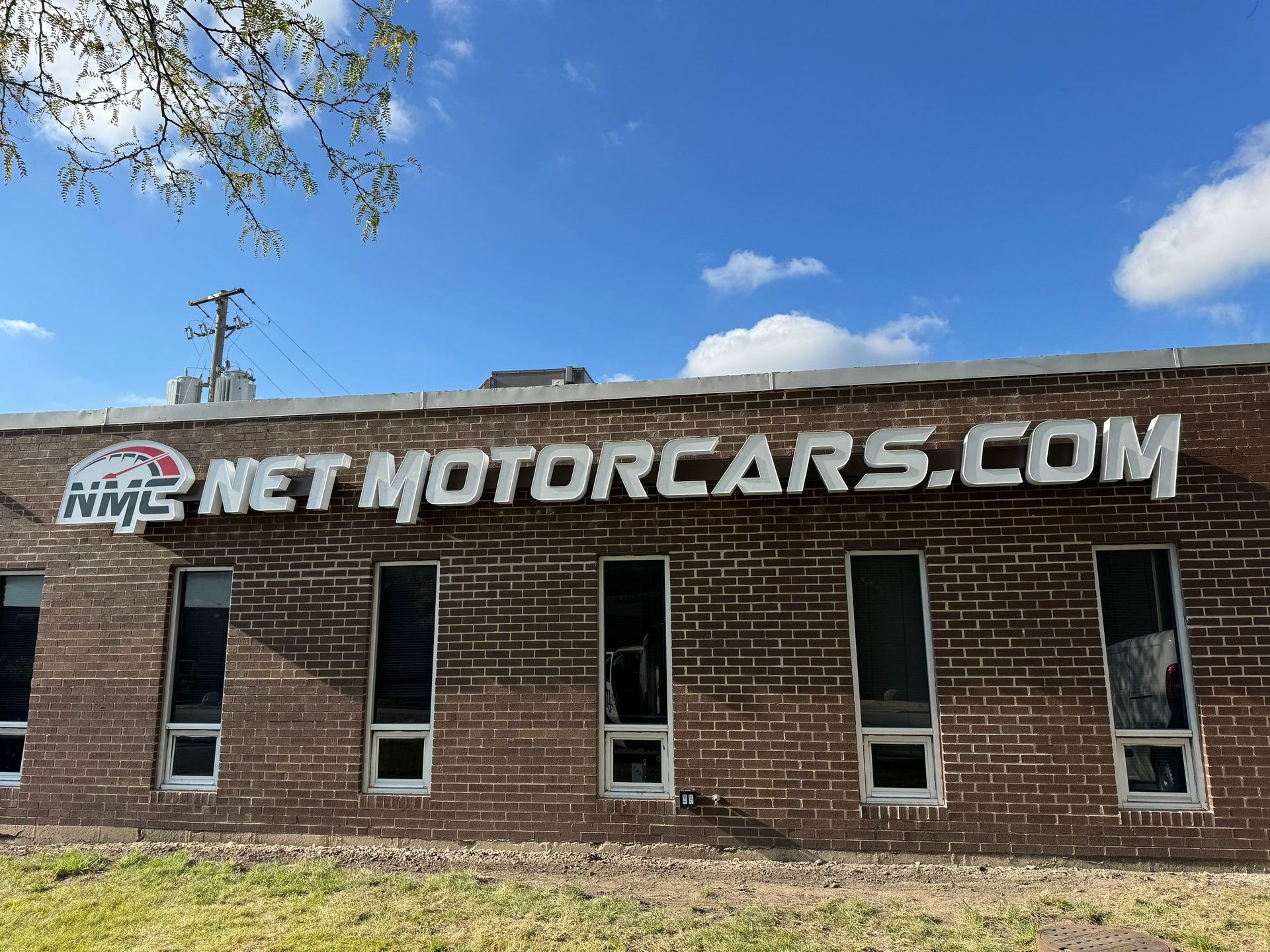 Brick building with a large NETMOTORCARS.COM sign and narrow windows under a blue sky