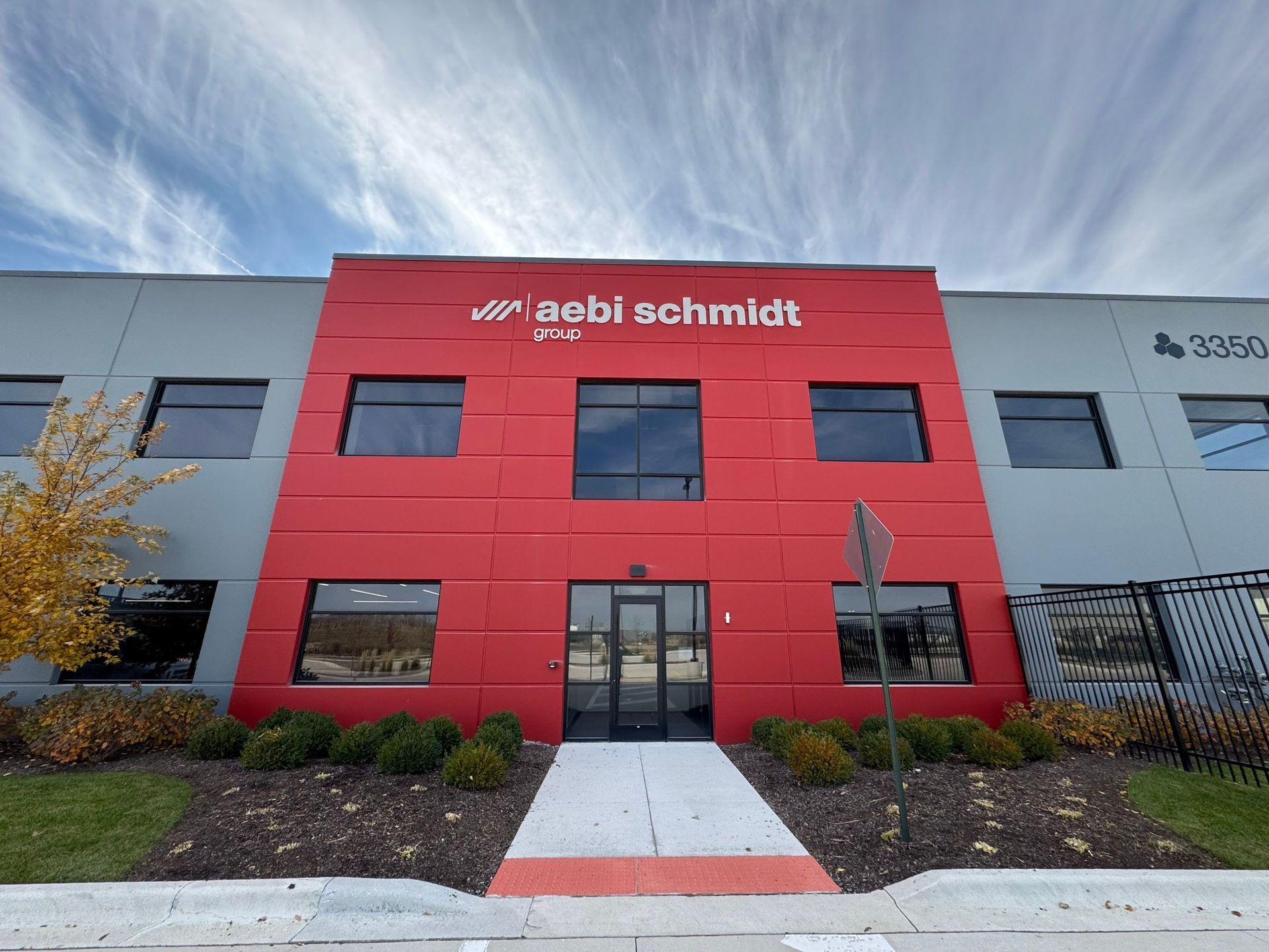 Red Zigbi Schmitt office building with glass doors, gray wings, and a walkway under a cloudy sky