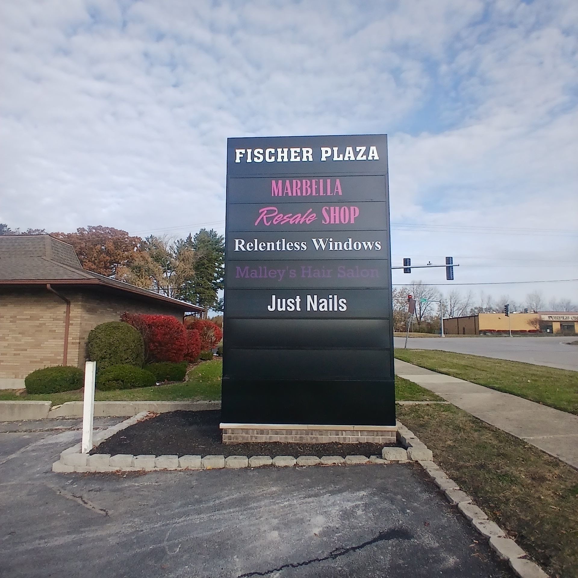 Pischer Plaza sign listing businesses, including Margarita House, Relaxing Windows, and Just Nails, beside a road