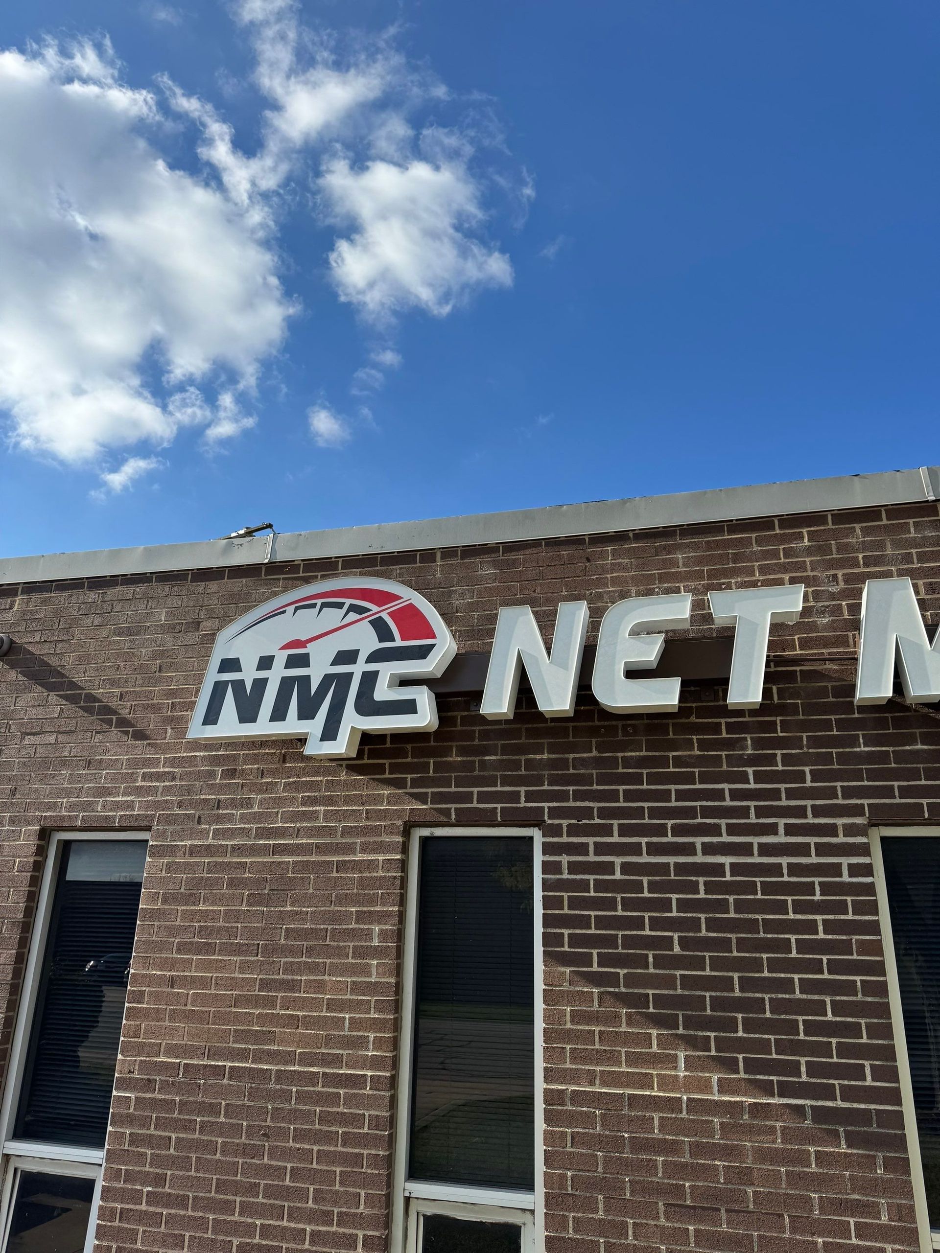 Brick building with NMC Net logo sign against a blue sky with clouds