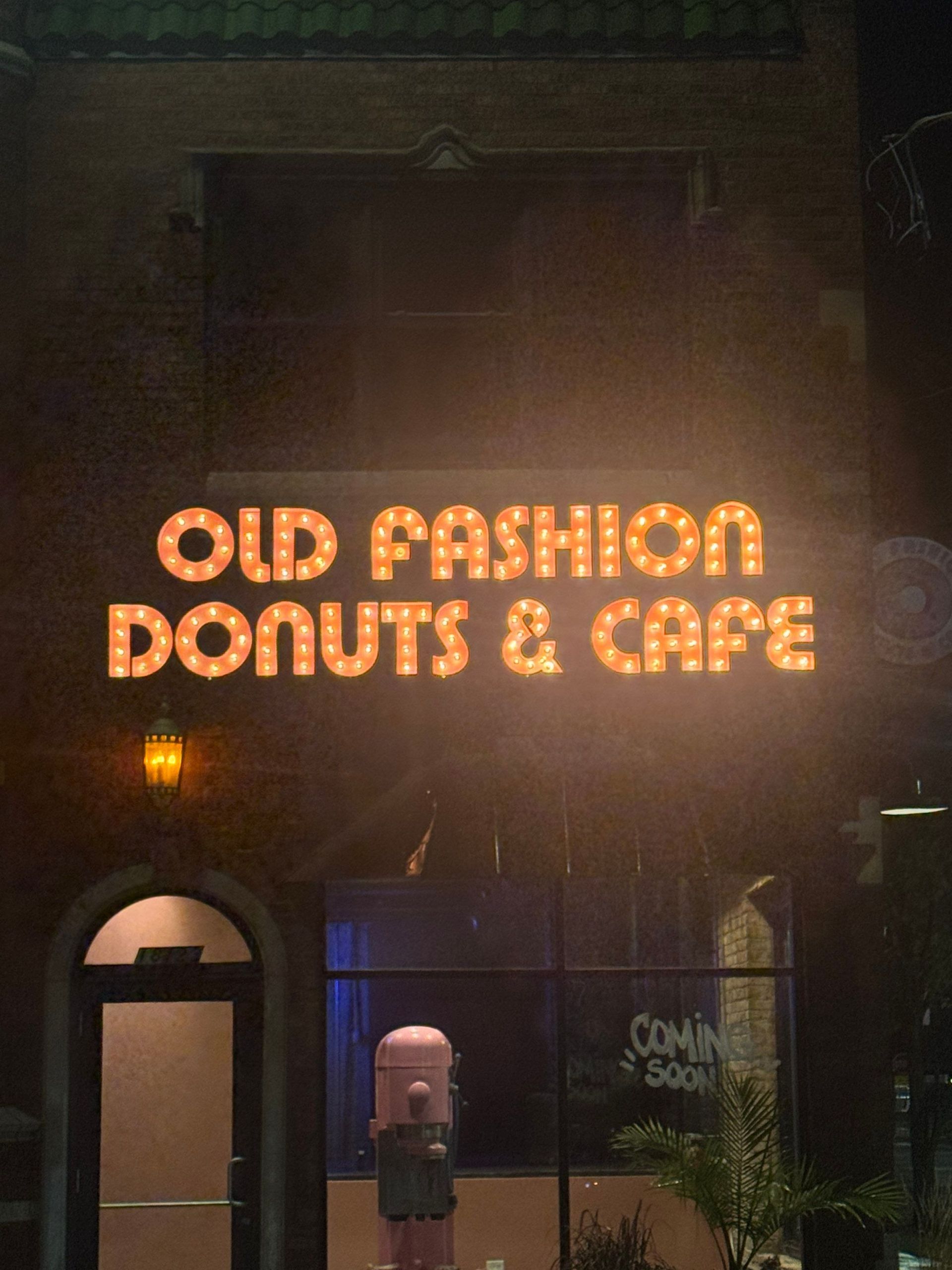 Neon sign for “Old Fashion Donuts & Cafe” above a dark storefront at night.