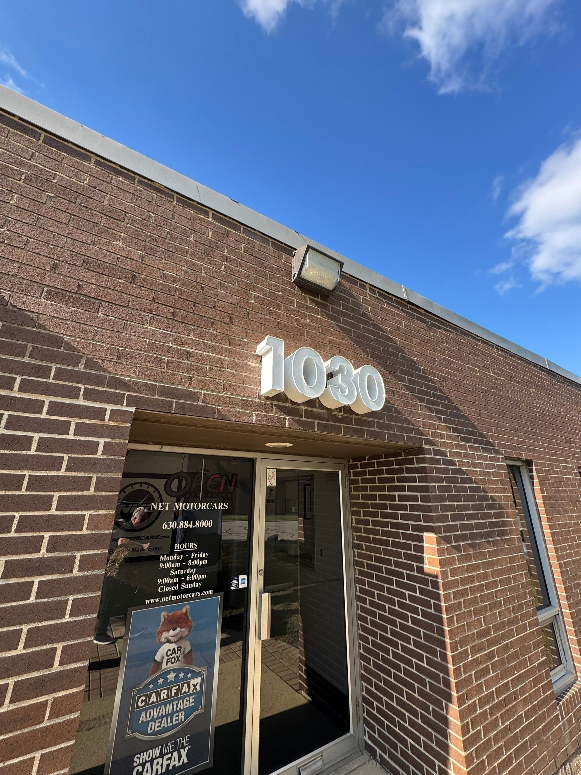 Brick storefront entrance with glass door, sign reading “1000,” and blue sky overhead