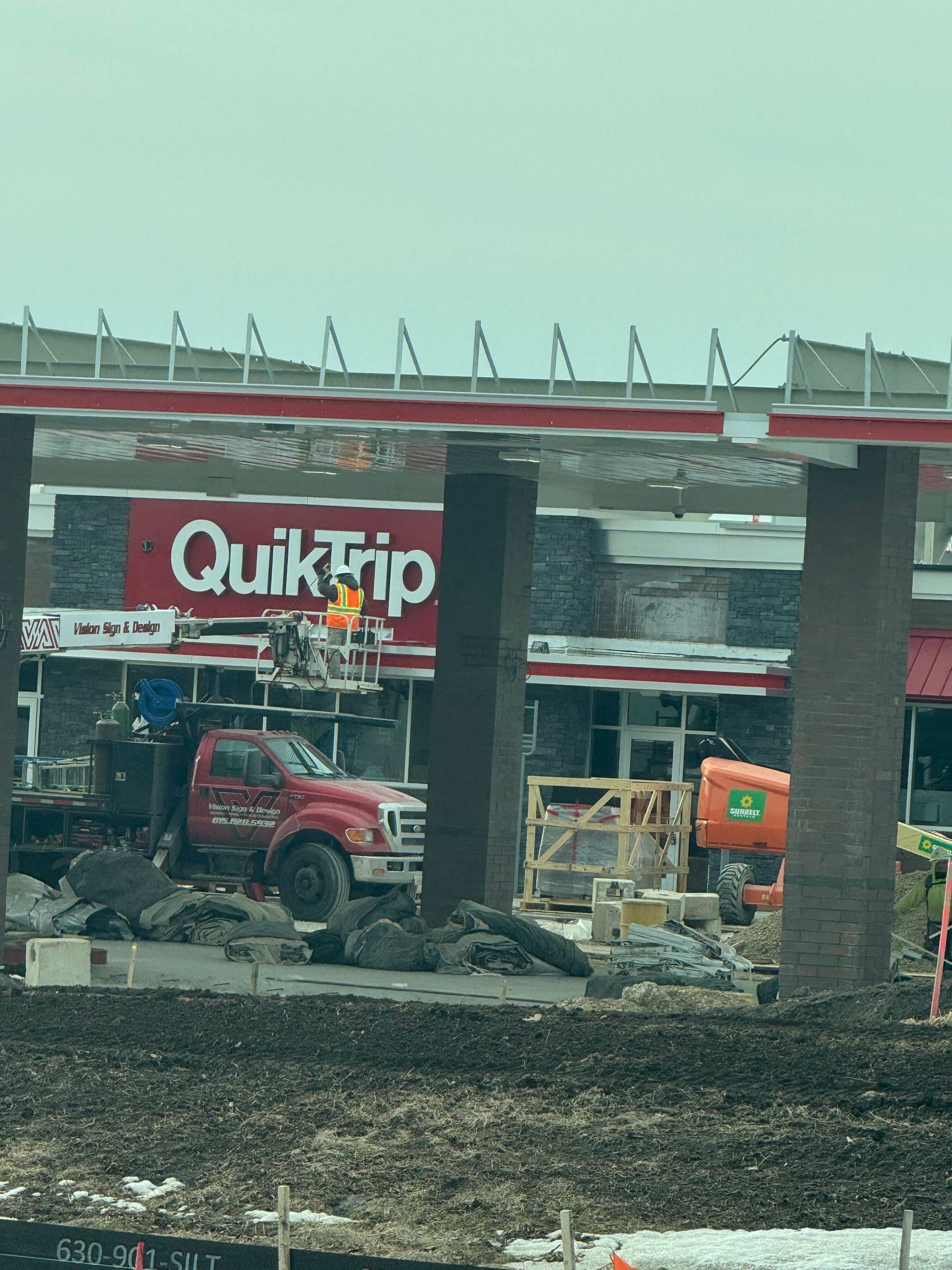Construction equipment outside a QuikTrip, with debris and a red truck in front of the store.