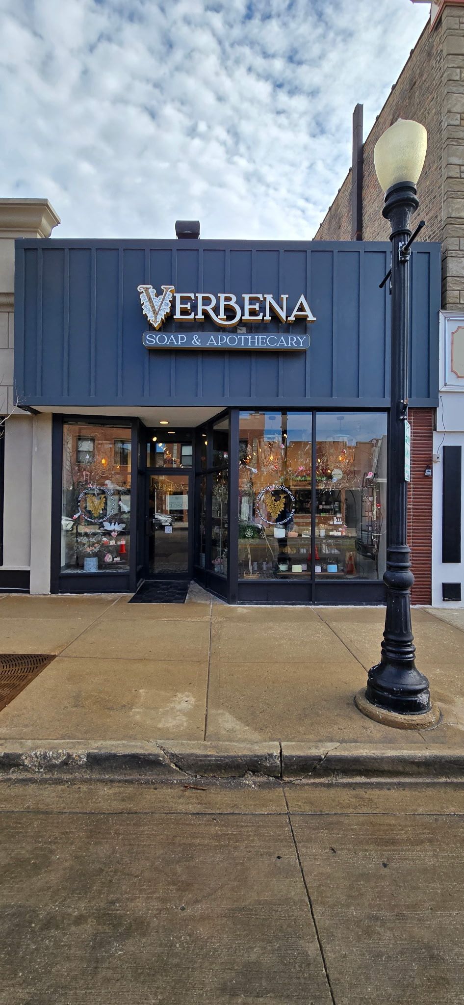 Storefront with a dark blue sign and large glass windows on a wet sidewalk.
