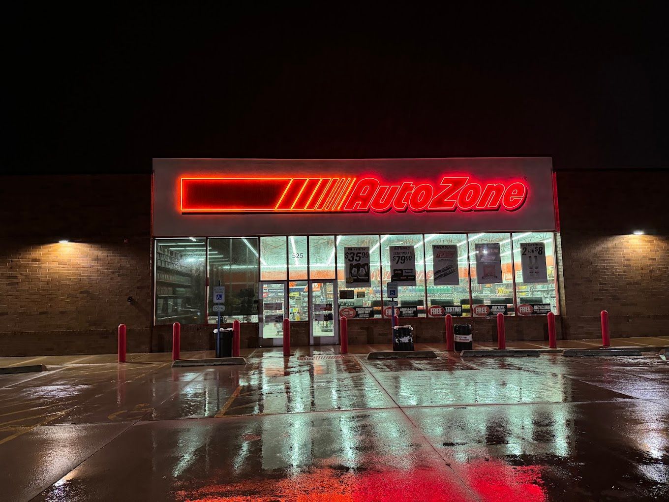AutoZone storefront at night with bright red neon sign and wet pavement reflecting lights