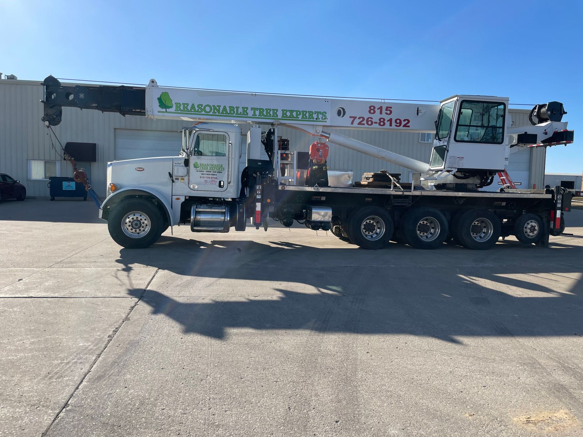 White crane truck with a flatbed parked outside an industrial building.