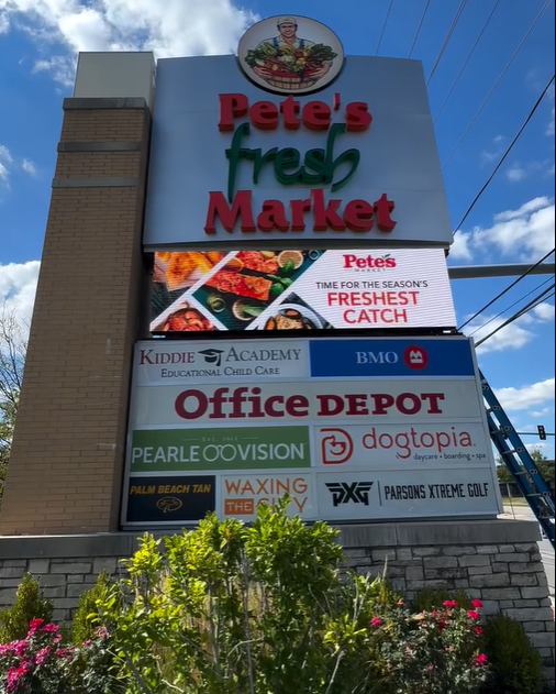 Pete’s Fresh Market storefront sign with multiple business logos against a blue sky