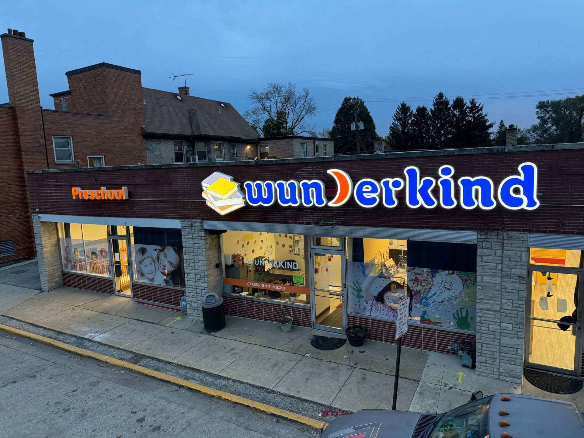 Storefront with a large “wunderkind” sign and lit interior on a brick street corner at dusk
