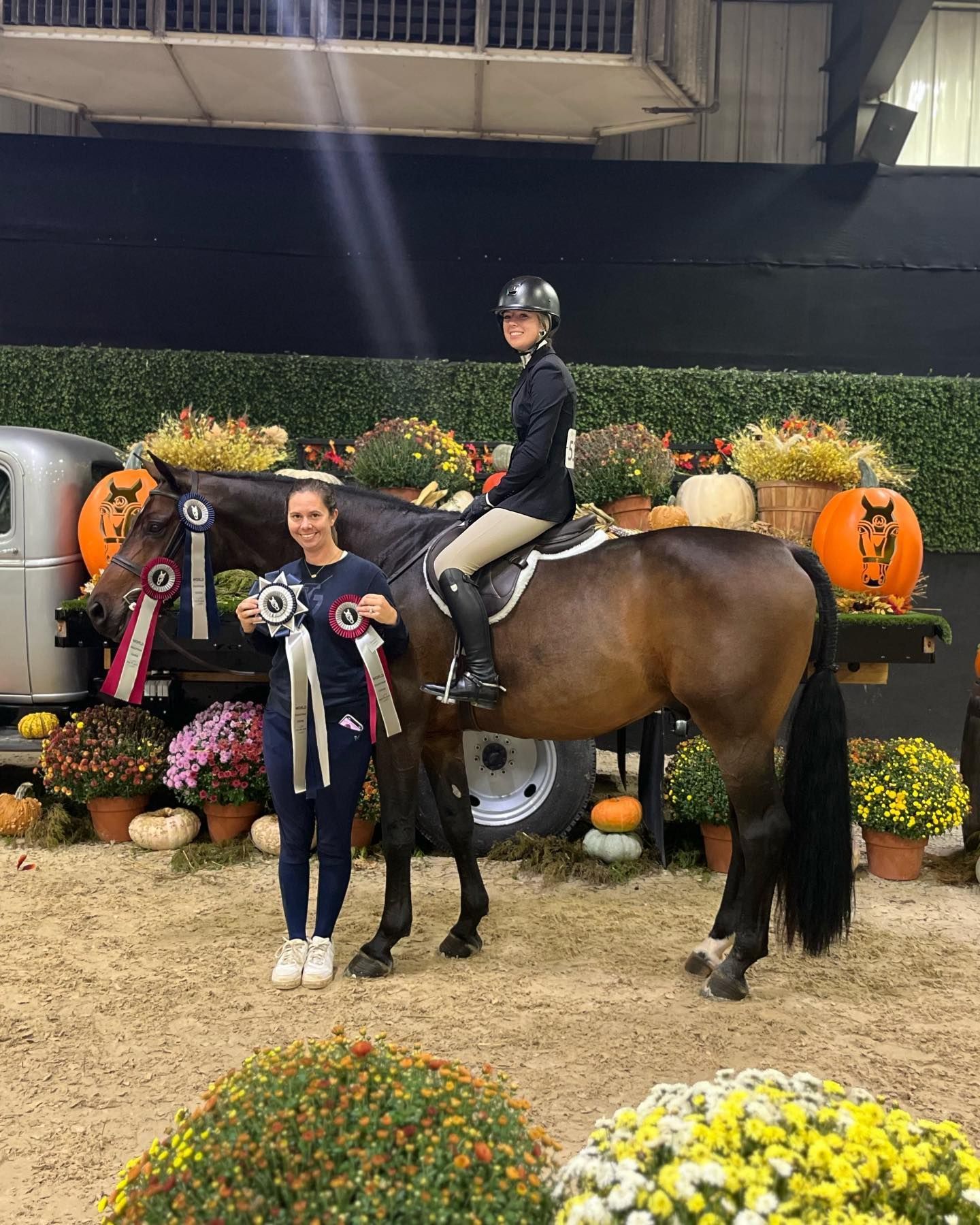A woman is standing next to a horse and holding a ribbon.