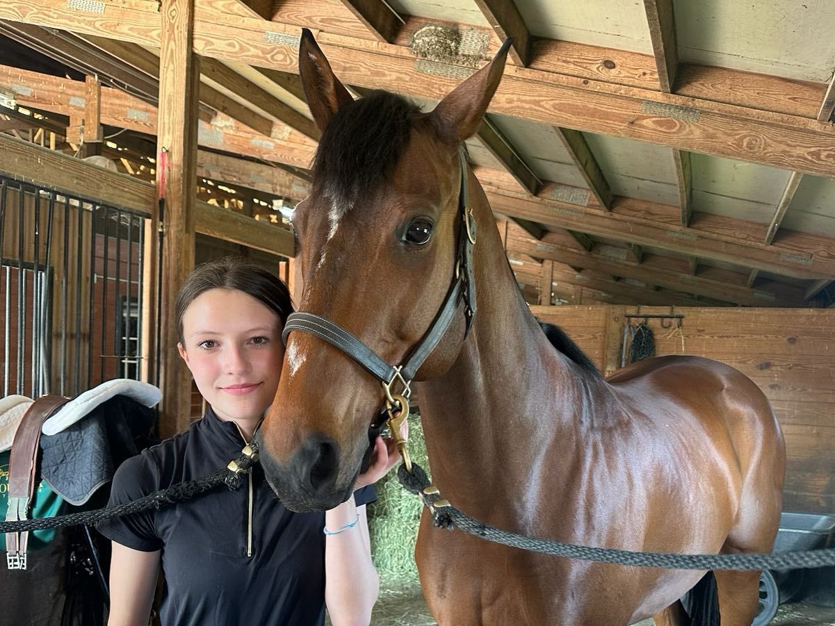 A woman is standing next to a brown horse in a stable.