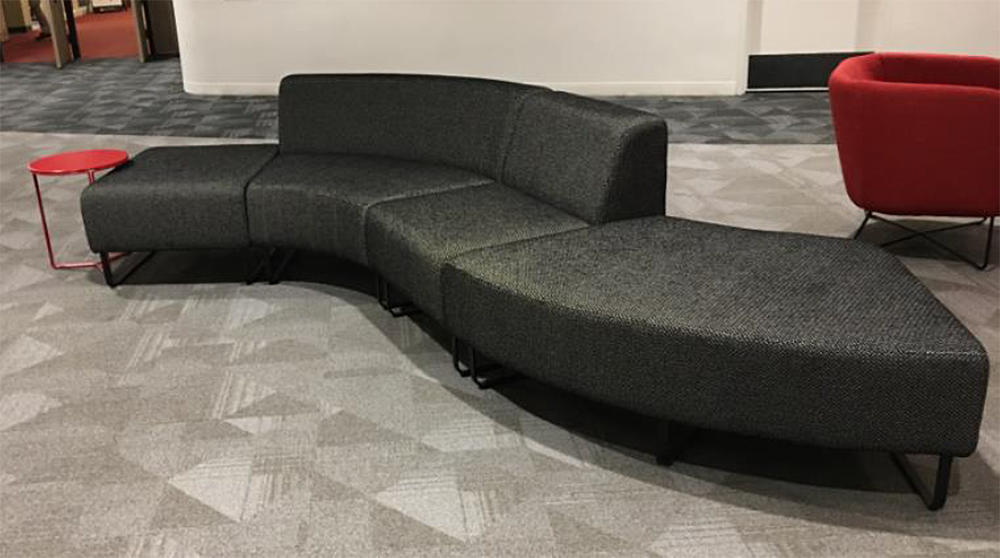 A curved couch is sitting in a waiting room next to a red chair.