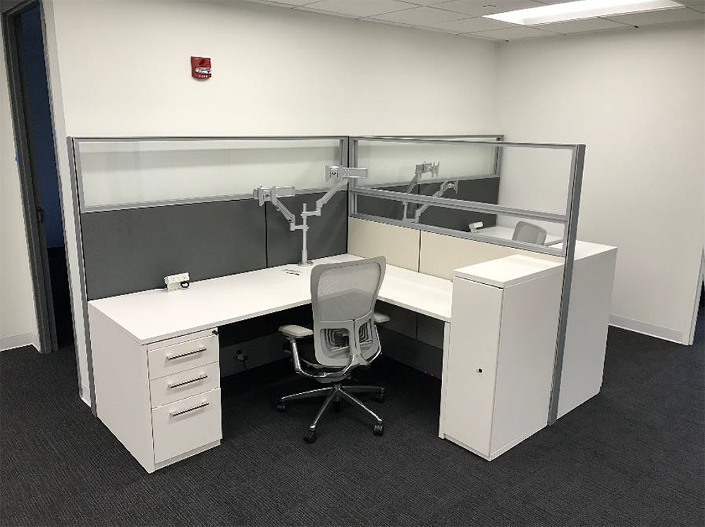 A cubicle with two desks and a chair in an office.