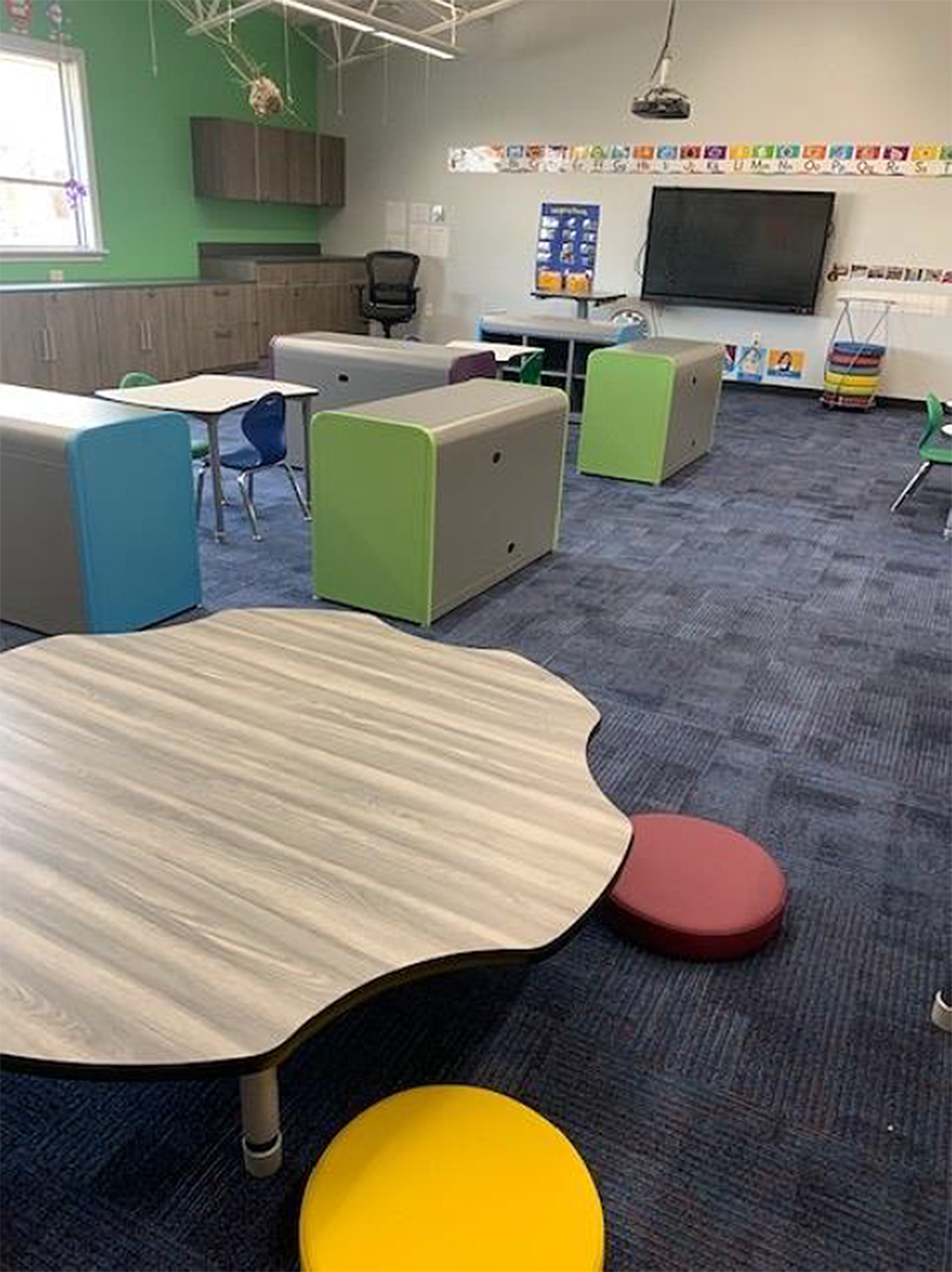 A classroom with tables , chairs , and a large screen.