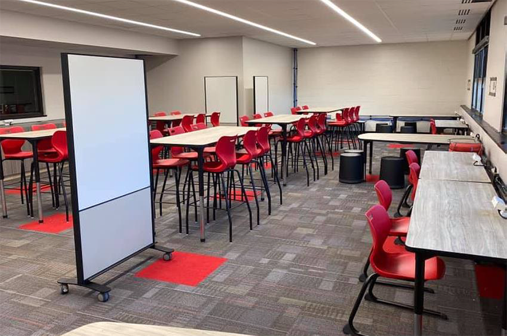 A large room with tables and chairs and a whiteboard.
