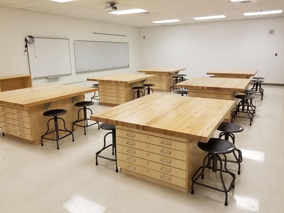 A classroom with wooden tables and stools and a whiteboard