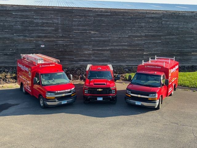 Three red vans are parked in front of a wooden wall.