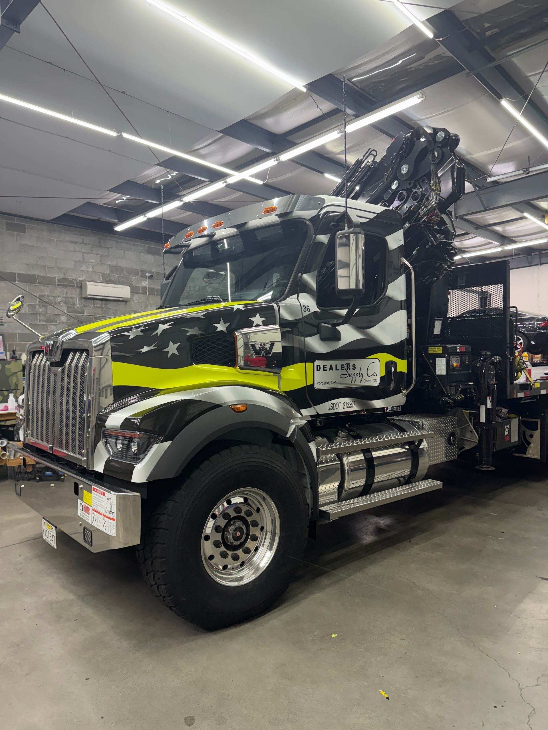 Black and yellow truck with crane parked inside a garage. The truck has an American flag design.