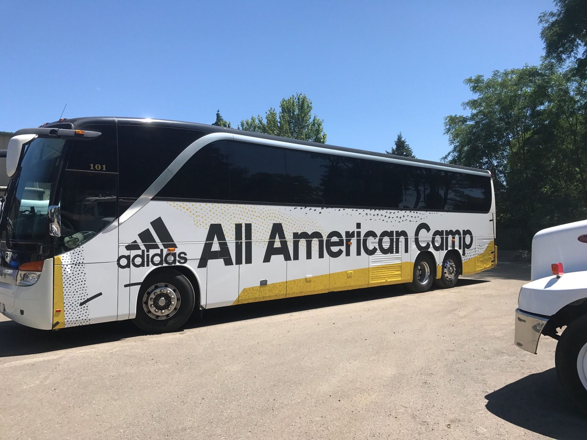 White bus with "adidas All American Camp" text, parked outdoors.