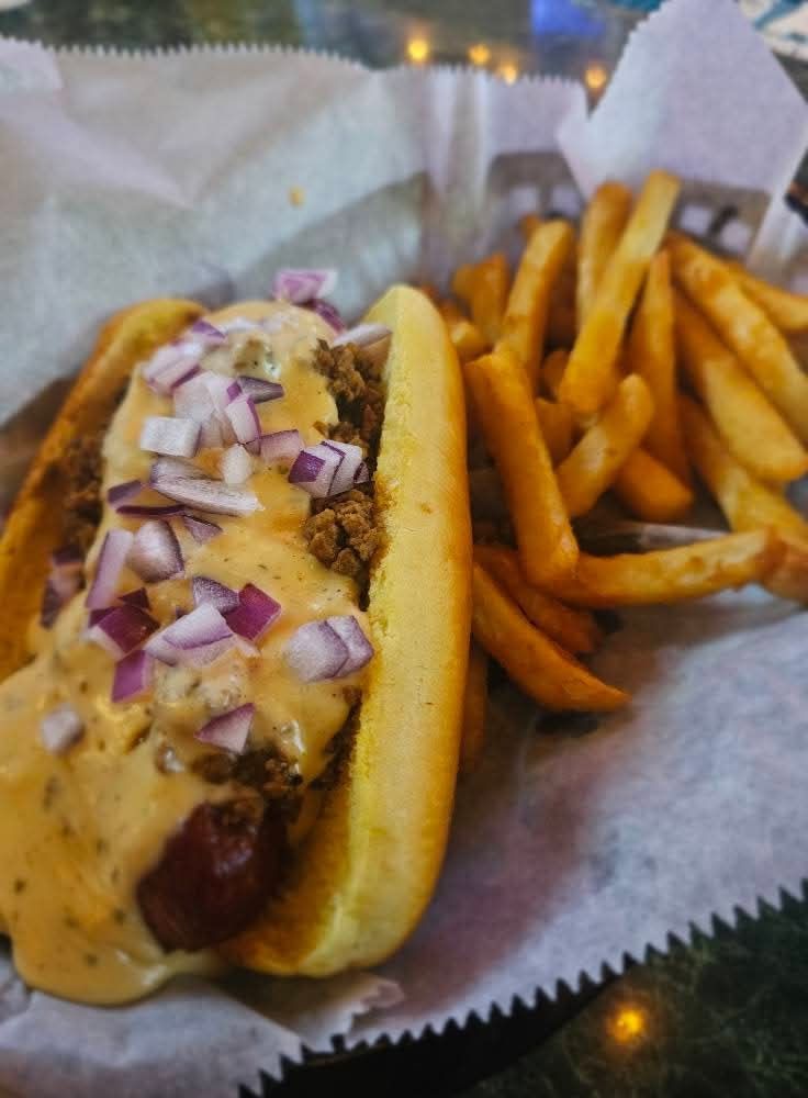 Hot dog with chili and onions next to fries in a basket.