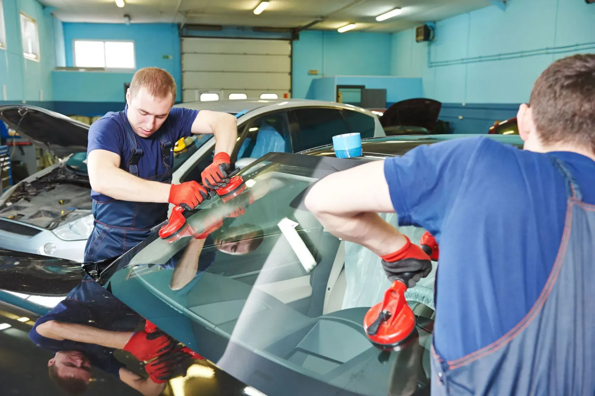 Two auto technicians installing a windshield in a repair shop, using suction cups.