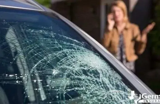 Cracked car windshield with woman in background on phone, gesturing with concern.