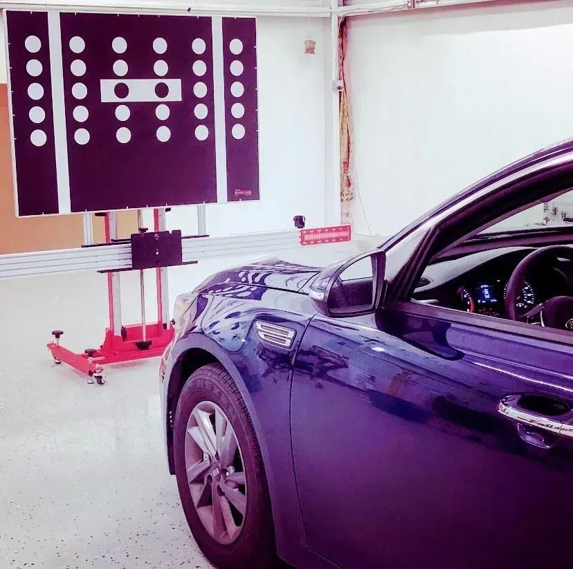 A blue car positioned in front of an alignment target in a garage.