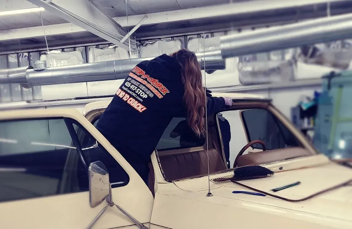 Person leaning into a cream-colored pickup truck, wearing a dark sweatshirt, in a garage.