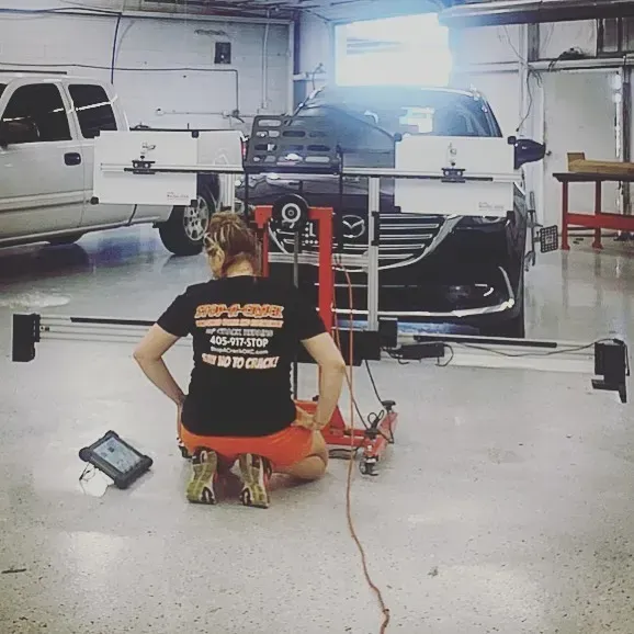 Person working on car alignment in a garage. Car is on lift, equipment in use.