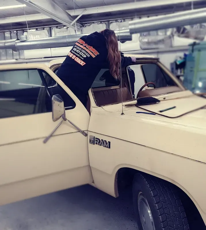 Person leaning into an open-doored beige Dodge Ram pickup truck. They are wearing a black sweatshirt.