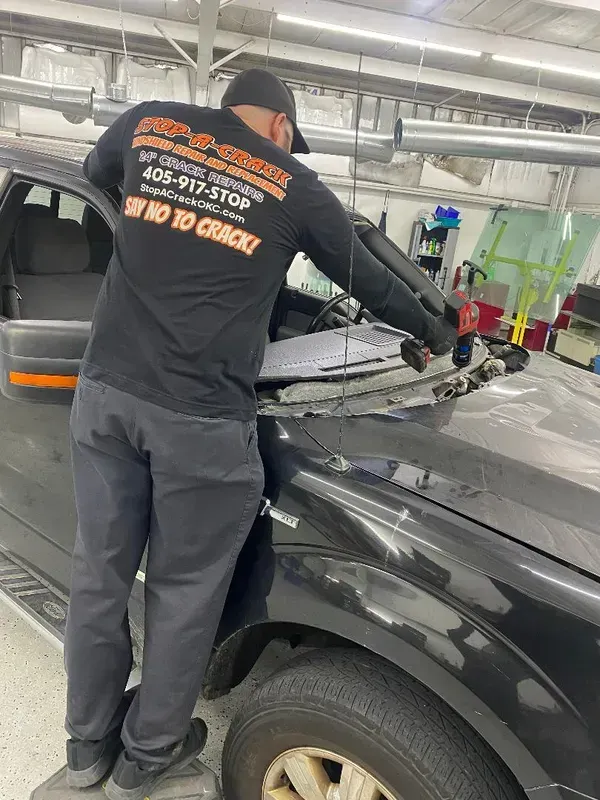 A person removing a windshield from a black pickup truck inside a repair shop.
