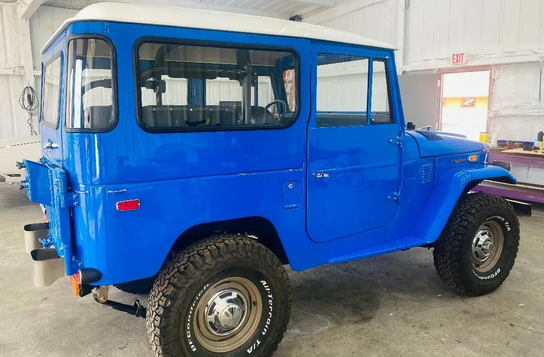 Blue and white vintage Toyota Land Cruiser with off-road tires, parked inside a building.