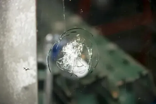 Shattered glass with radial cracks. Inside a structure, possibly a window. Bright, white light at impact point.