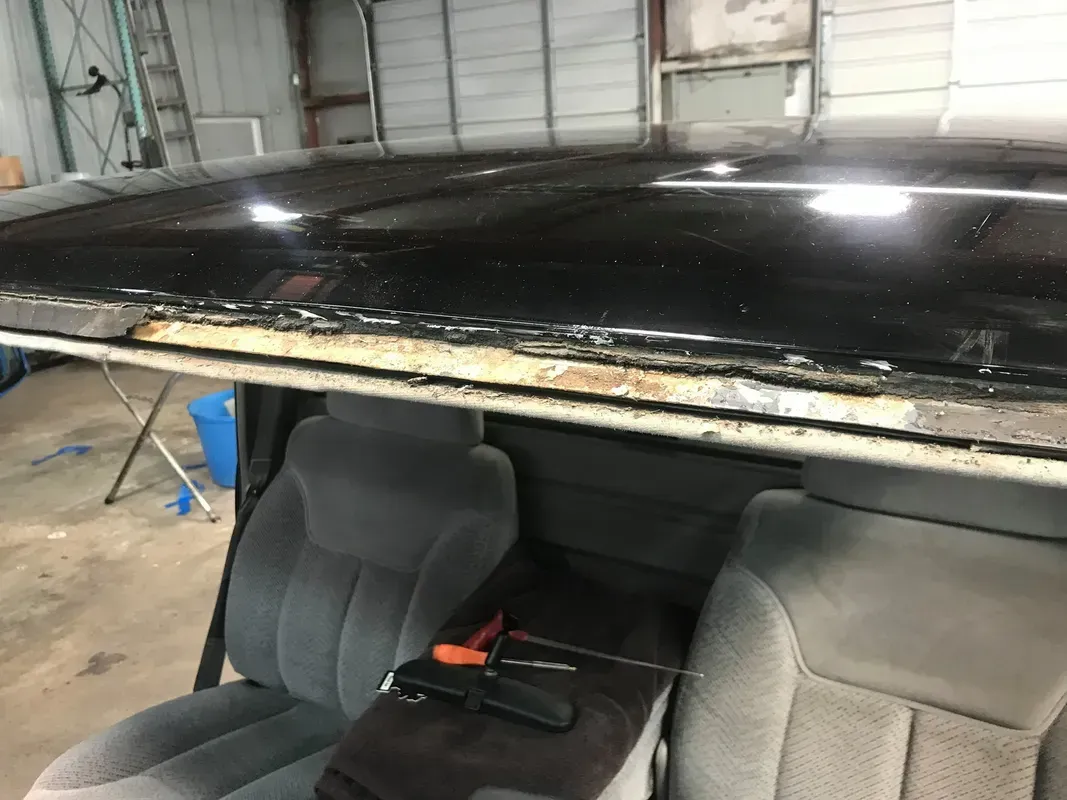Interior view of a pickup truck with black roof and gray seats. The roof shows signs of rust and damage.
