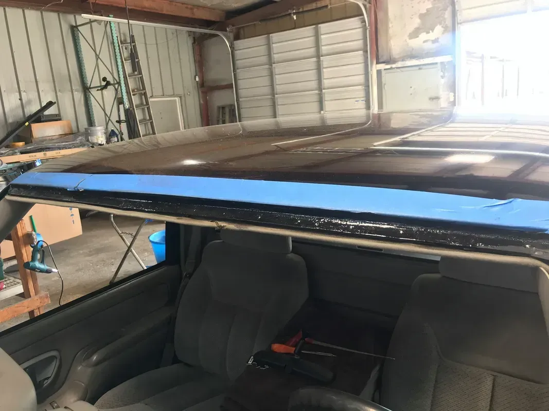 Interior view of a pickup truck with the roof removed for repair. Blue tape lines the windshield frame.